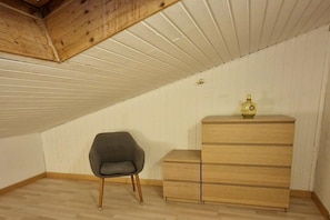 A room with a sloped ceiling, a wooden dresser with drawers, and a single chair. - Holiday apartment Ariane (Garmisch-Partenkirchen)