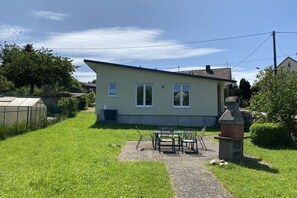 A single-story house with a paved patio area, a small table with chairs, and a statue. - Holiday home with 2 bedrooms (Nohfelden OT Eckelhausen)