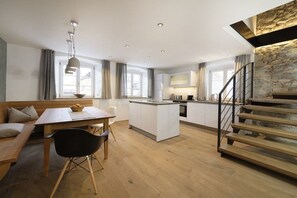 A modern kitchen with a central island, wooden flooring, and a staircase with a stone accent wall. - Heimat1883 - Coachman (Garmisch-Partenkirchen)