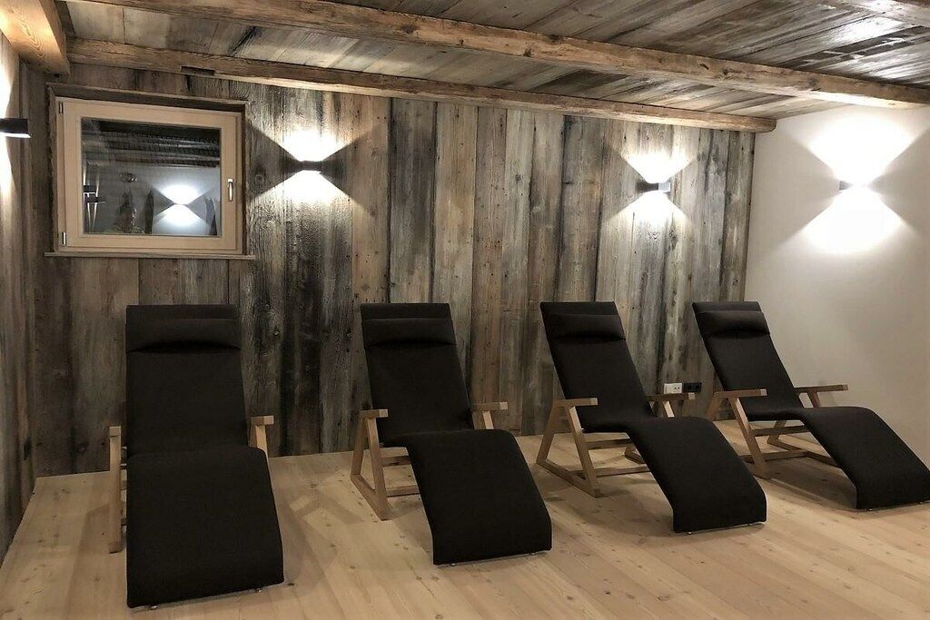 Une pièce aux murs en bois, avec un tableau encadré et quatre fauteuils noirs.