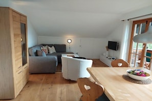 A cozy living space with a sofa, ottoman, dining table, and a TV. - Holiday apartment Spitzenblick (Garmisch-Partenklirchen)