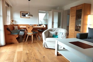 A cozy living room with a wooden floor, a sofa, a dining table, and a kitchen area visible through an open door. - Holiday apartment Spitzenblick (Garmisch-Partenklirchen)