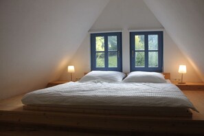 A bedroom with a sloped ceiling, two windows, a bed with white bedding, and bedside lamps. - Goldberg Forest Lodge (Bad Harzburg)