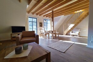A spacious living area with a high ceiling, wooden beams, a sofa, a TV, and a staircase leading to an upper level. - Goldberg Forest Lodge (Bad Harzburg)