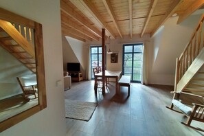 A spacious loft with high ceilings, exposed wooden beams, a dining area with a table and chairs, a television, and a large window providing natural light. - Goldberg Forest Lodge (Bad Harzburg)