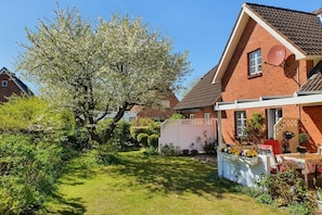 A residential property with a brick house, a garden with a large tree, and a patio area with outdoor furniture. - Holiday apartment with 1 bedroom (Rendsburg)