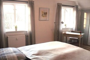 A bedroom with a bed, a desk with a chair, a radiator, and a window with curtains. - Holiday apartment with 1 bedroom (Rendsburg)