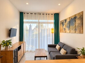 A modern living room with a sofa, a coffee table, a TV mounted on the wall, and a large window with curtains. - New Listing (Soustons)