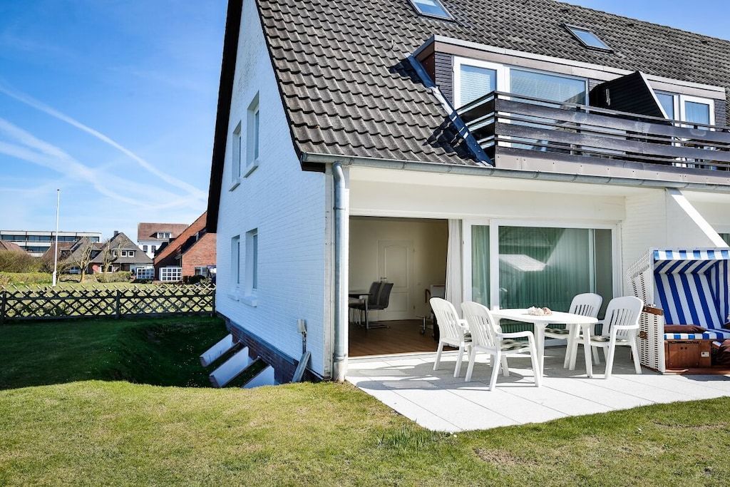 Ein modernes Haus mit einer überdachten Terrasse, einem Essbereich mit weißen Stühlen und einem großen Fenster.