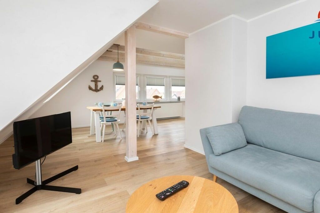 A modern living room with a flat-screen TV, a sofa, and a dining area with a table and chairs.