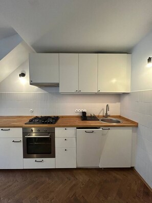 A modern kitchen with white cabinetry, a wooden countertop, a built-in oven, and a stainless steel sink. - Lumina 2BR Apt in the Center I 8 guests (Warszawa)