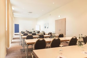 Une salle de conférence équipée de plusieurs tables et chaises, d’un tableau blanc et d’une porte.