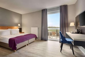 Habitación de hotel con cama, escritorio, silla, televisor y vista al exterior.