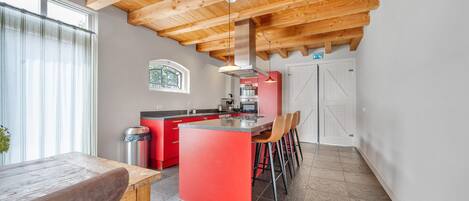 A modern kitchen with a central island, red cabinetry, and a dining area with a wooden table.