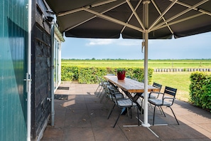 An outdoor patio with a table and chairs, a large umbrella, and a view of a green field. - Farmhouse Retreat for 20 Guests in Snelrewaard (Snelrewaard)
