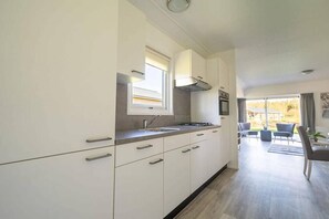 A modern kitchen with white cabinetry, a window above the sink, and a view of the outdoor patio area. - Charming Chalet Near Efteling (Kaatsheuvel)