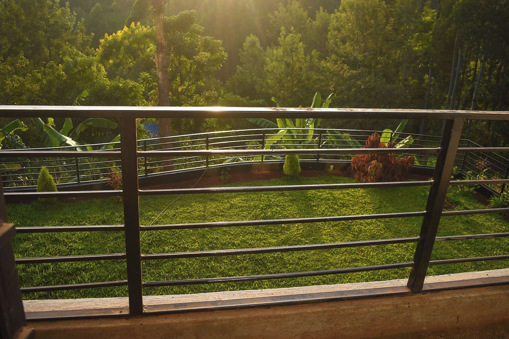 A view through a metal railing with a grassy area, trees, and a small bridge.
