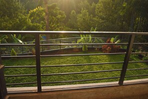 A view through a metal railing with a grassy area, trees, and a small bridge.