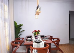 Ein Essbereich mit einem Holztisch, gedeckt für sechs Personen, einer Hängelampe und einem Blumentopf.