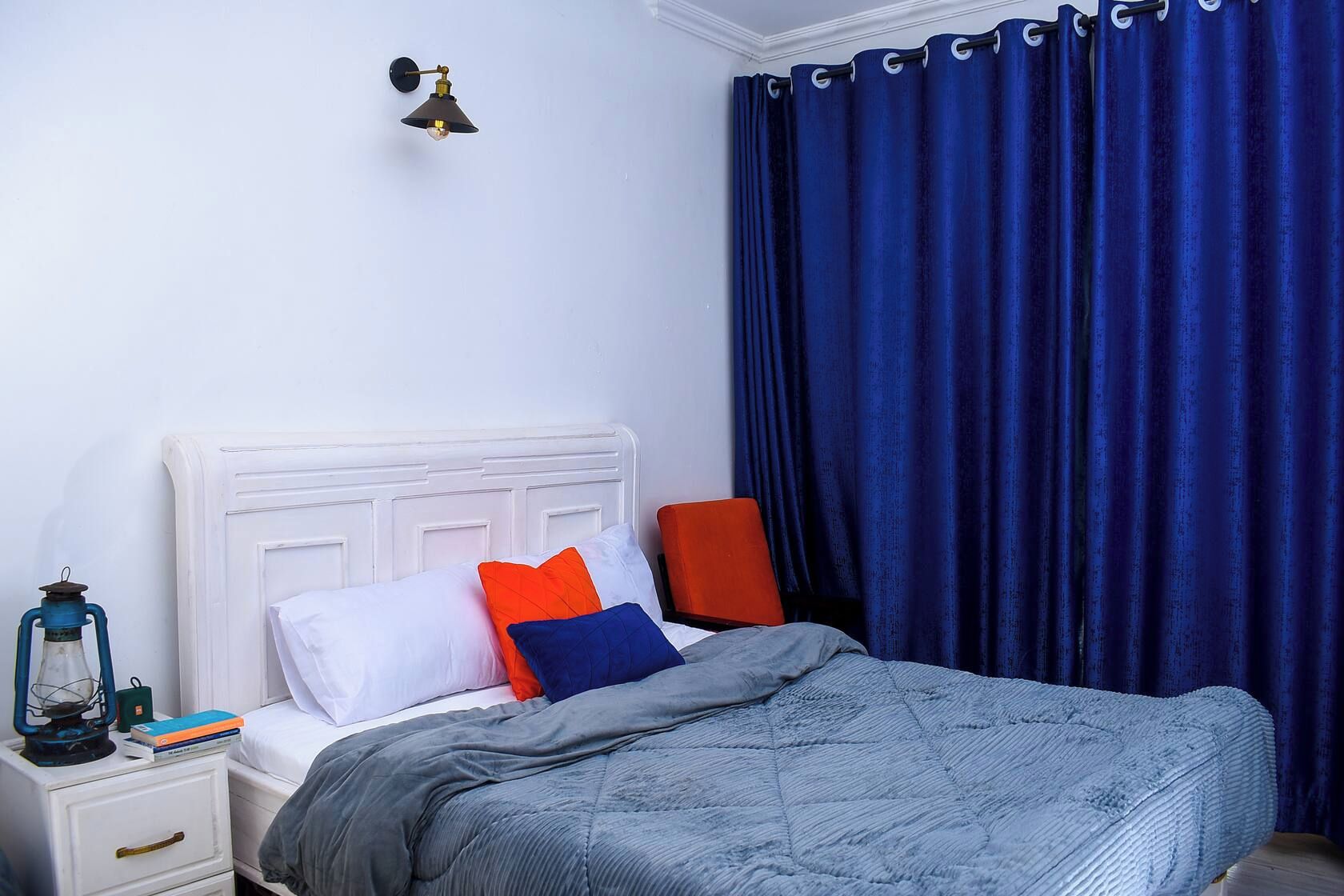 A bed with a white headboard, a blue blanket, and two pillows in orange and blue.