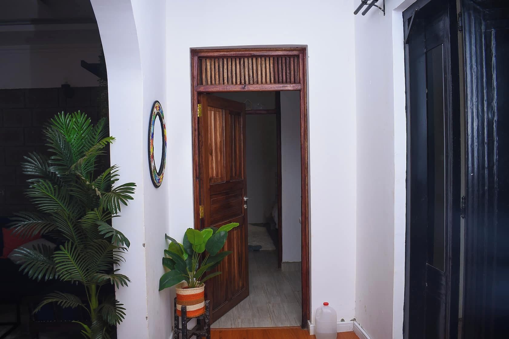 Un couloir avec une porte en bois, une plante en pot et un objet décoratif fixé au mur.