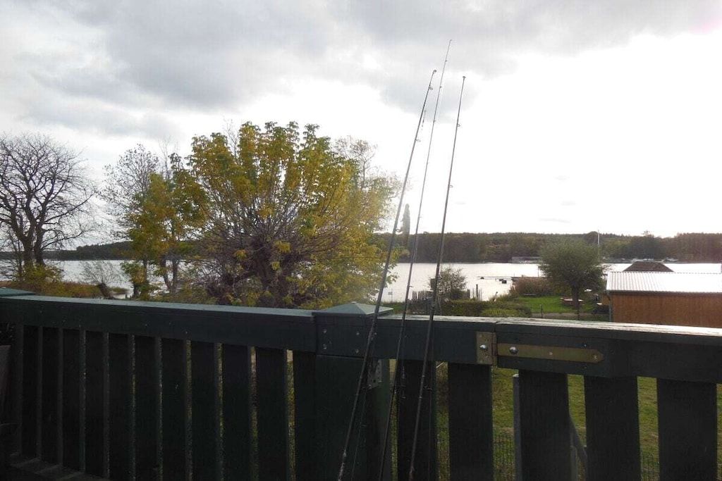 A view from a balcony with a railing, overlooking a body of water, trees, and a distant building.