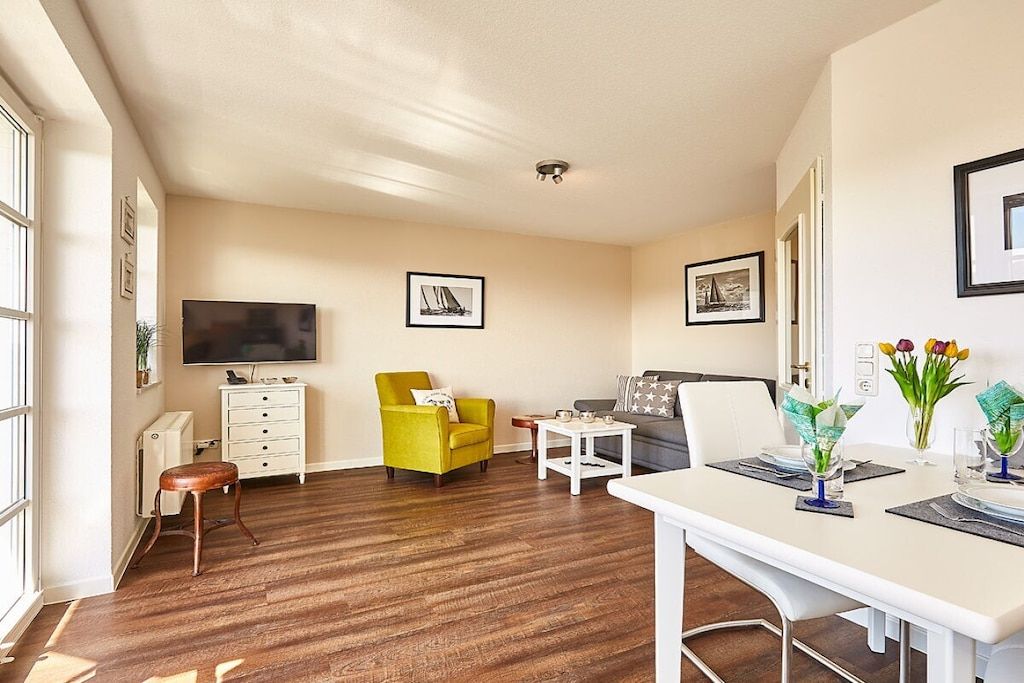 Ein modernes Wohnzimmer mit Flachbildfernseher, einem gelben Sessel, einer Couch, einem Esstisch mit Stühlen und einem Kamin.