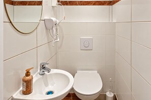 A bathroom with a sink, toilet, and a hairdryer on a wall-mounted stand. - Vienna Days Sofa Nights 1BR near Westbahnhof (Vienna)