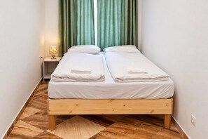 A double bed with white linens and towels, a bedside lamp, and a wooden floor with a geometric pattern. - Vienna Days Sofa Nights 1BR near Westbahnhof (Vienna)