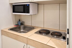 A kitchen with a microwave, sink, and two stovetops. - Vienna Days Sofa Nights 1BR near Westbahnhof (Vienna)