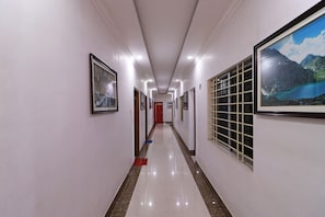 A corridor with framed pictures on the walls, a red door at the end, and a window with a view of mountains. - Hotel O Misti Inn (Jamshedpur)