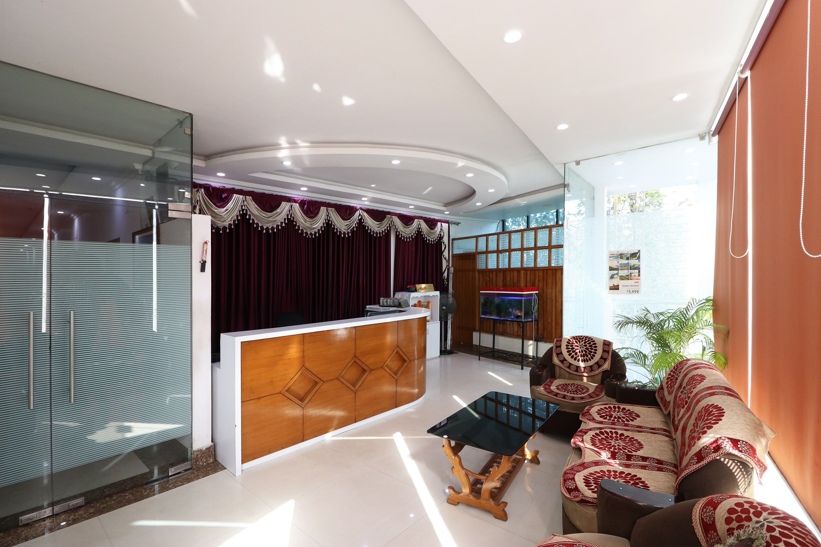 A modern reception area with a wooden reception desk, a glass partition, and a seating area with patterned cushions.
