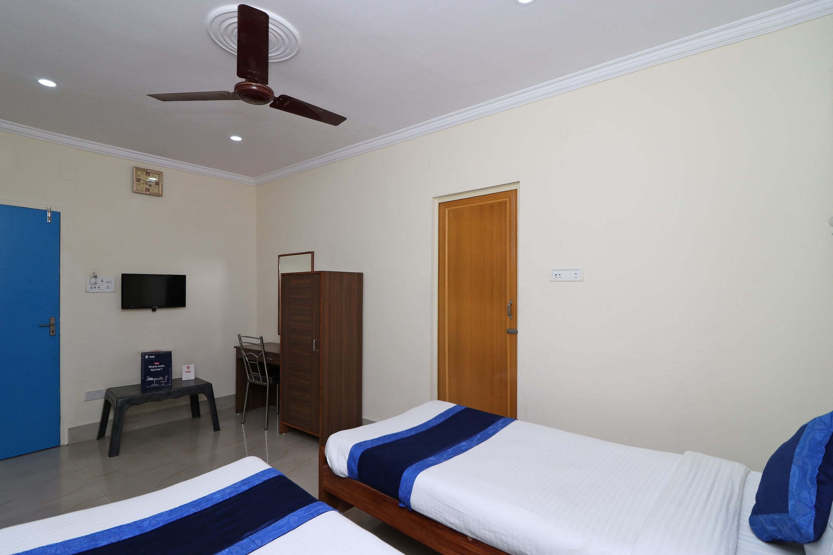 Habitación de hotel con dos camas, un escritorio, un armario, un televisor y un ventilador de techo.