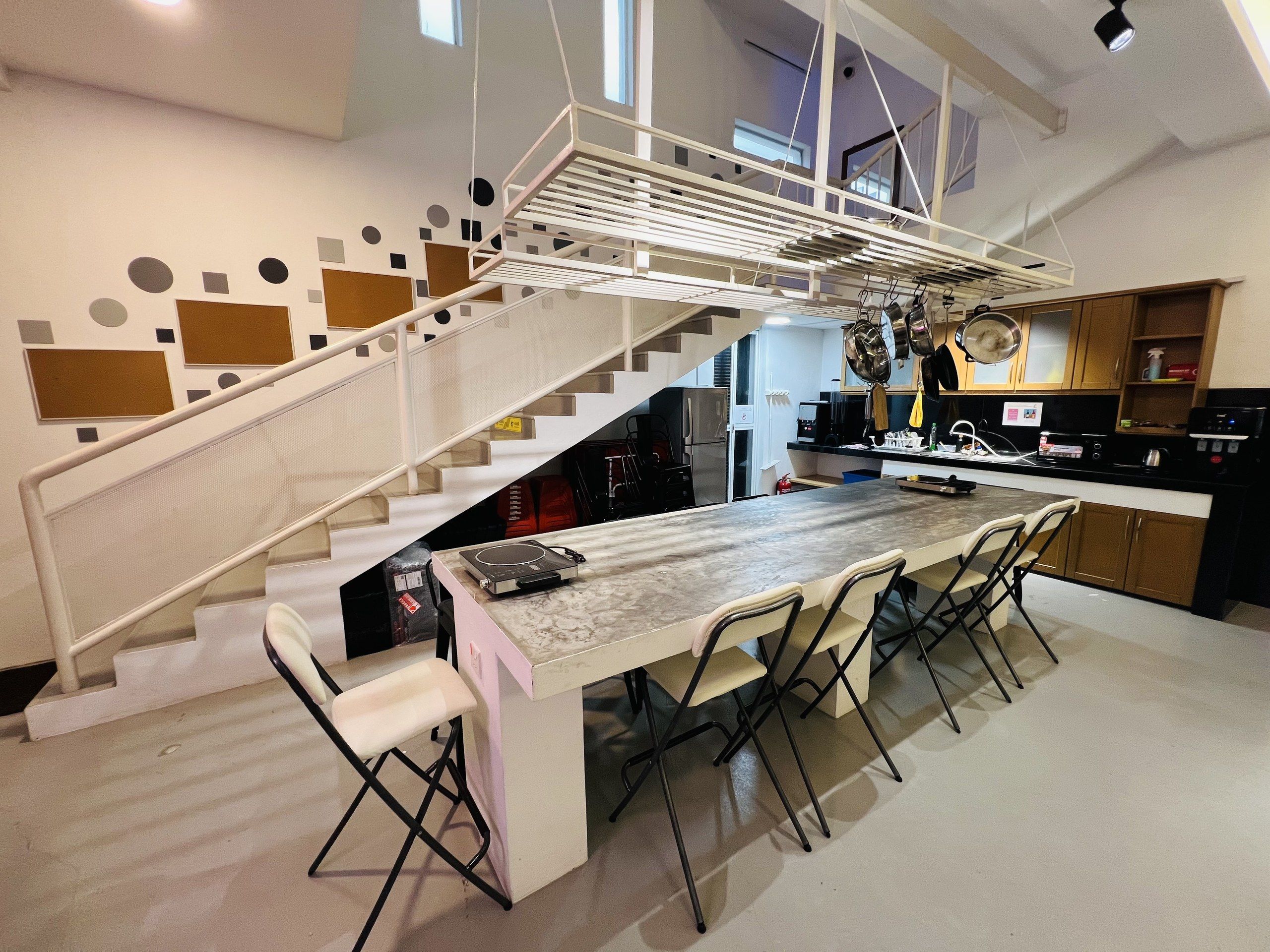 Una cocina moderna con una isla central, una zona de comedor con sillas y una escalera de diseño singular.