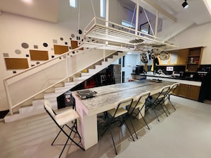 A modern kitchen with a central island, a dining area with chairs, and a staircase with a unique design.