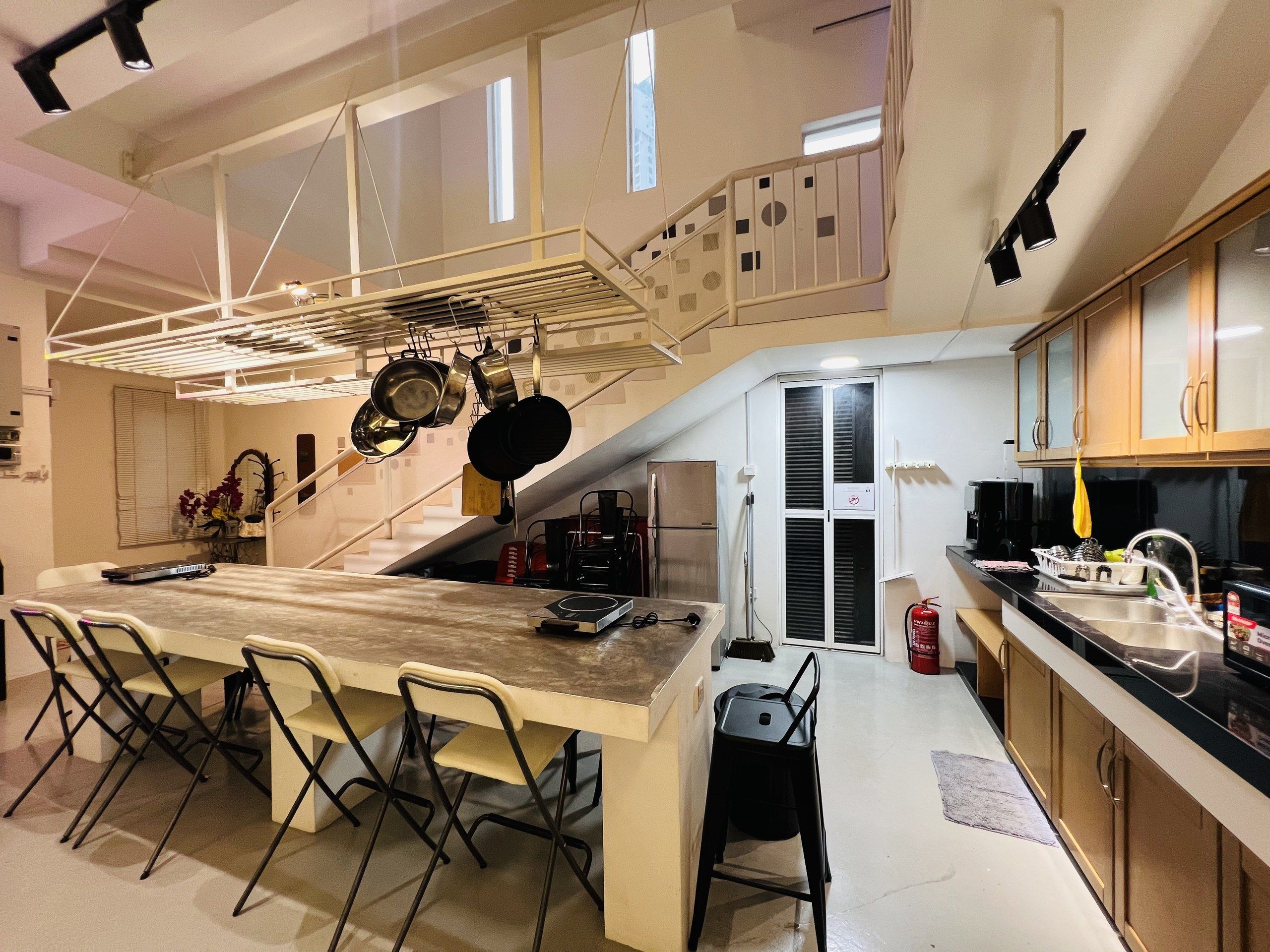 Cocina compacta con una isla central, comedor con sillas y una escalera que sube a un nivel superior.