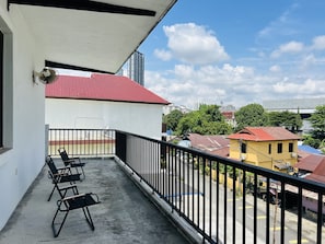 Uma varanda com piso de concreto, guarda-corpo de metal preto e cadeiras pretas.