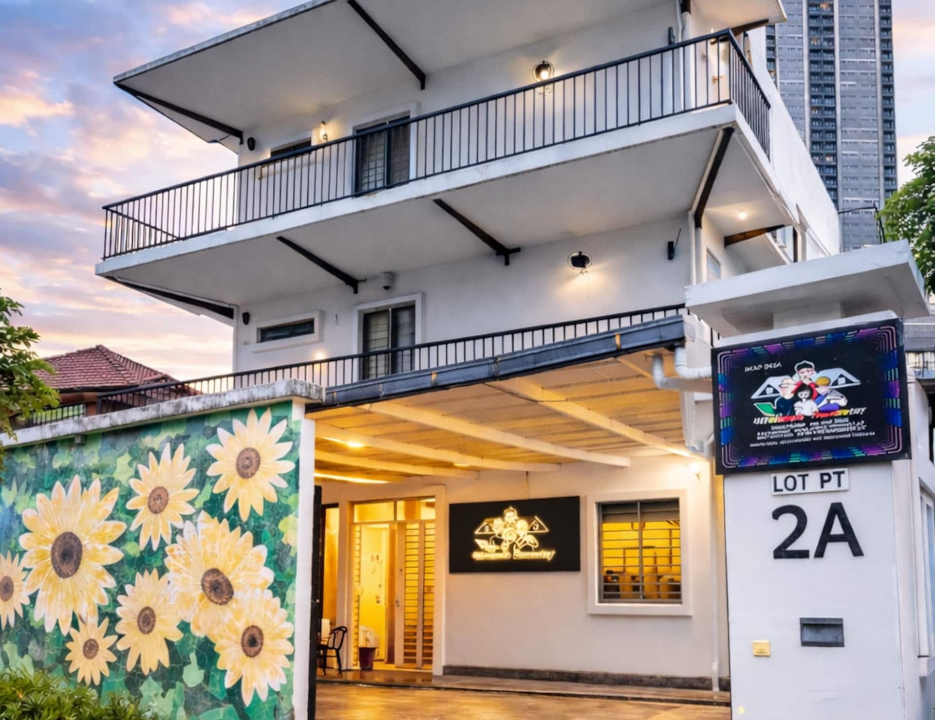 A modern two-story building with a balcony, a mural of sunflowers on the facade, and a sign indicating 'LOT PT 2A'.