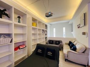 A hotel room with a bed, a sofa, a bookshelf, and a projector.