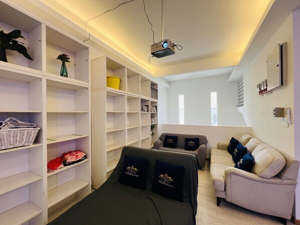A hotel room with a bed, a sofa, a bookshelf, and a projector.