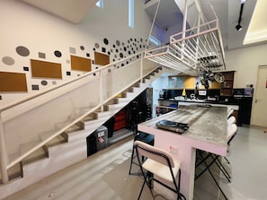 Cozinha moderna com ilha central, escada de design geométrico e área de jantar com banquetas.