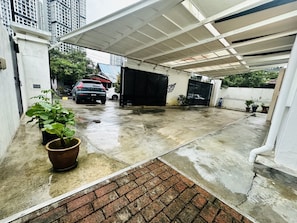 A covered outdoor parking area with a wet concrete floor, a brick entrance, and potted plants.