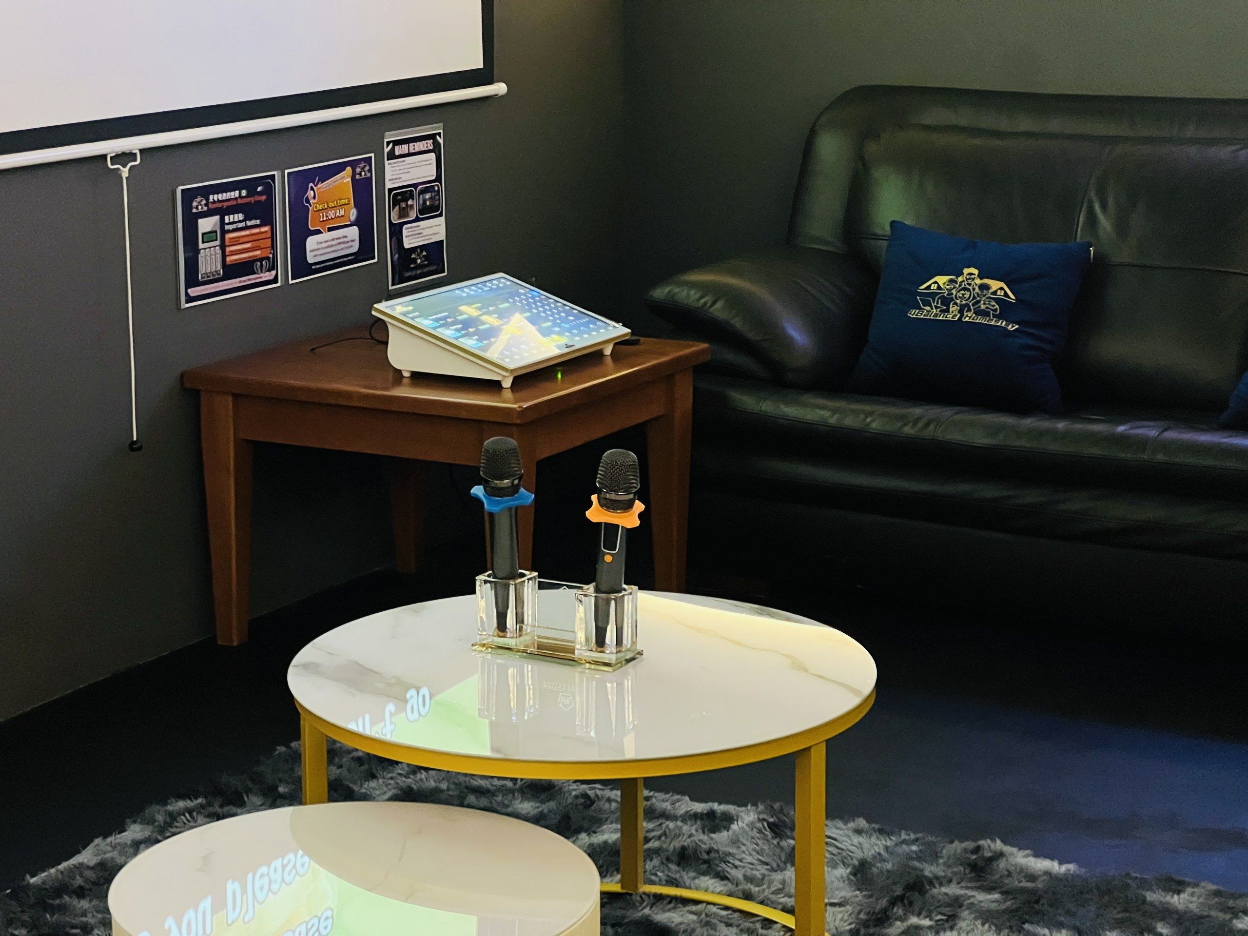 A conference room with a white table, two microphones, a projector screen, and a leather couch with a blue pillow.
