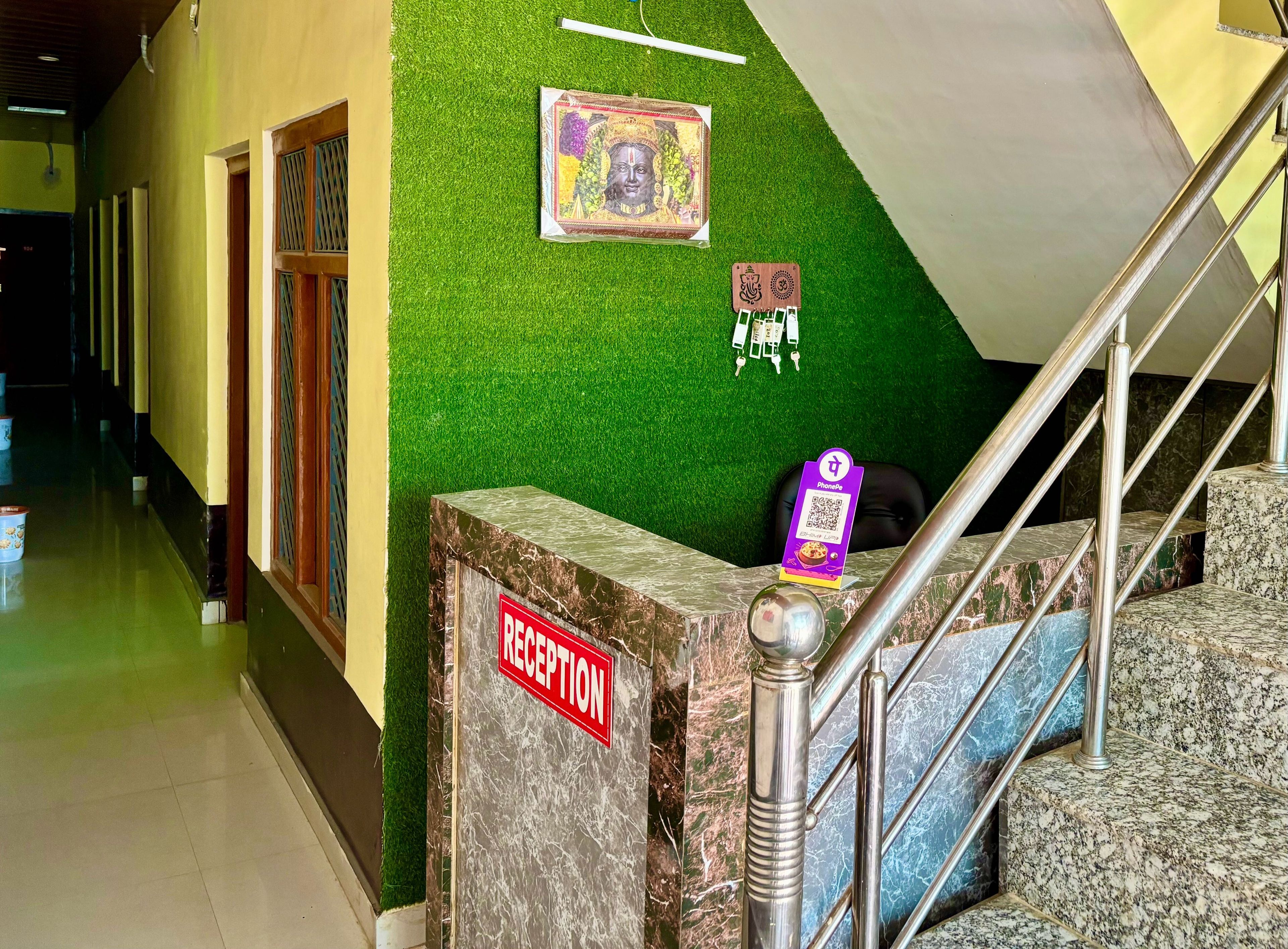 A reception area with a marble reception desk, a staircase with metal railings, and a green wall with a framed picture.