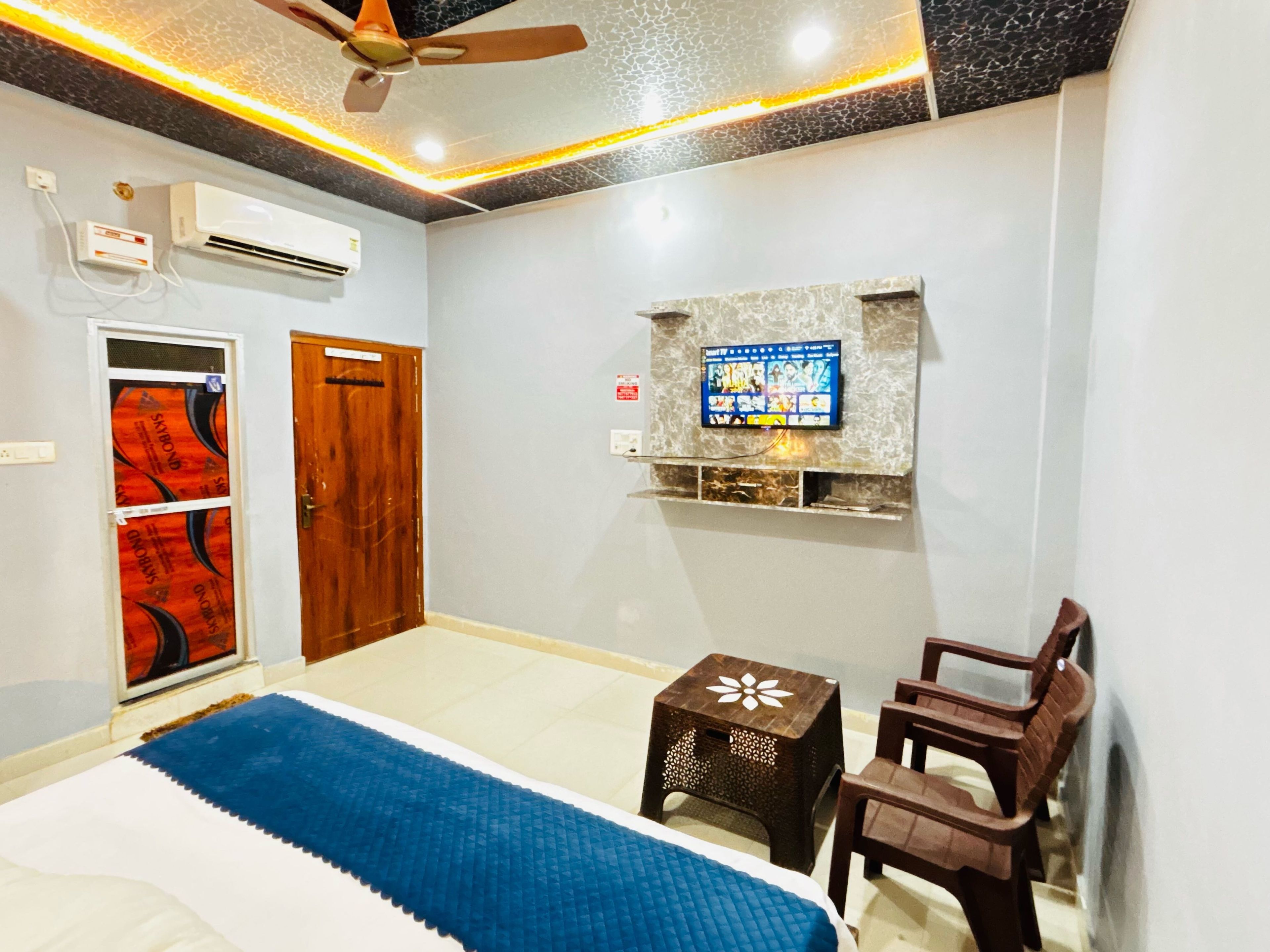 A bedroom with a bed, a TV mounted on the wall, a ceiling fan, and a wooden door.
