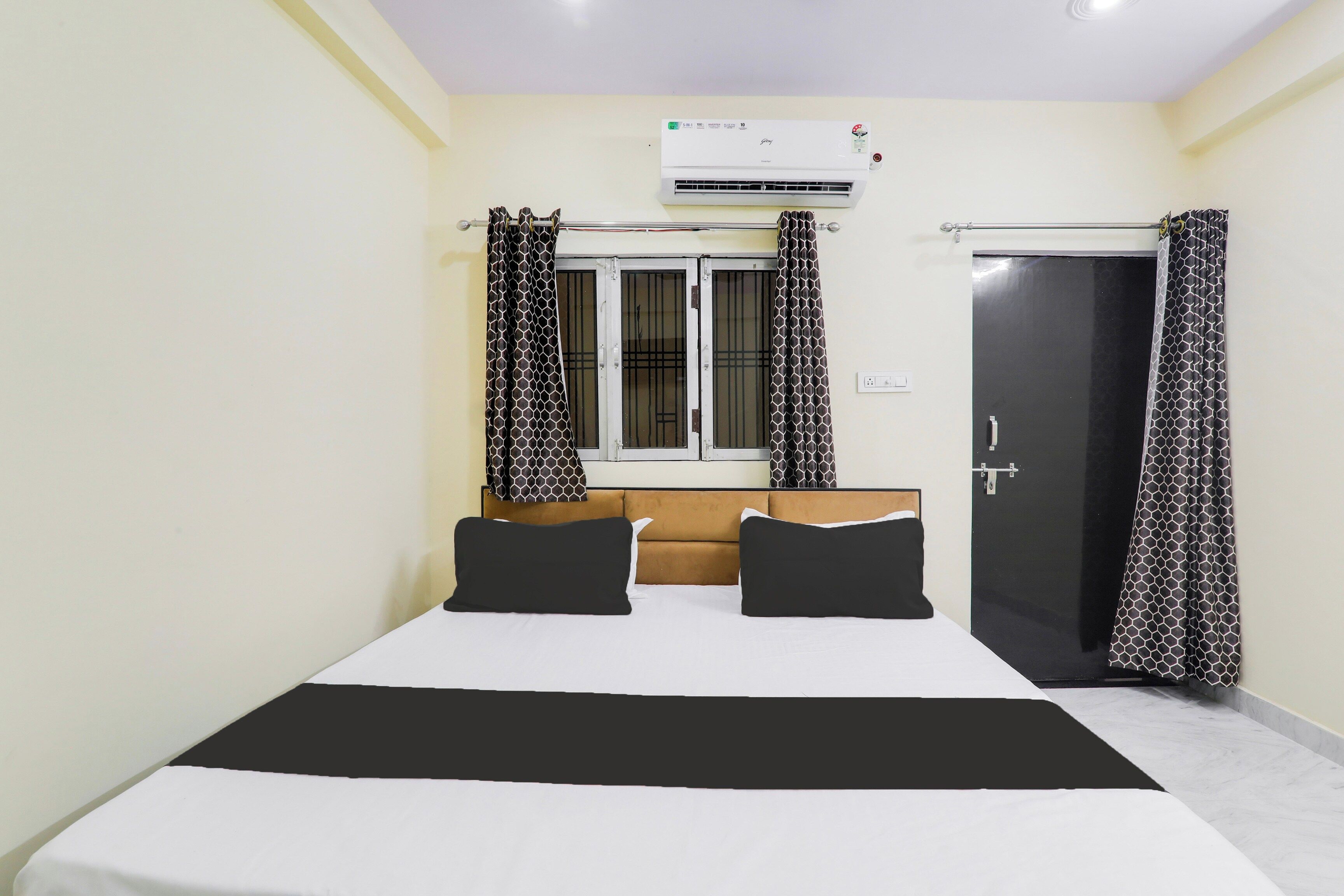Ein Hotelzimmer mit Bett, einem Fenster mit Vorhängen, einer Klimaanlage und einer Tür.