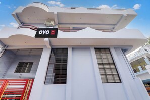 Un hotel llamado 'OYO Hotel Raman' con un diseño arquitectónico moderno, que presenta columnas verticales destacadas y grandes ventanales.