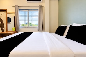 Een hotelkamer met een groot bed, een televisie op een houten standaard, een raam met gordijnen en uitzicht op groen.