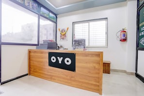 Een receptiebalie met een bordje met de tekst 'OYO' in een hotellobby met ramen, een brandblusser en een ingelijst kunstwerk.