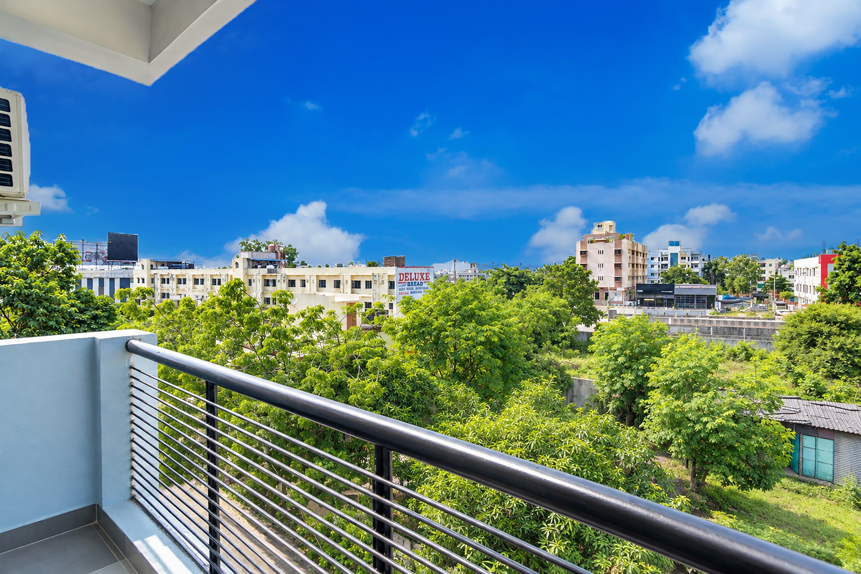 A balcony with a metal railing overlooking a cityscape with various buildings and greenery.